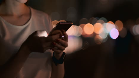 Close-up-of-a-mobile-phone-in-the-hands-of-a-girl-presses-her-fingers-on-the-screen-in-the-night-city-on-the-background-of-a-beautiful-bokeh.-Young-businessman-girl